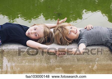 "Little girls lying together beside pond, holding hands" View Large Photo Image Stock Photo - "Little girls lying together beside pond, holding hands". Fotosearch
