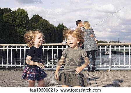 Little girls playing outdoors while their parents kiss in the background View Large Photo Image Stock Photography - Little girls playing outdoors while their parents kiss in the background. Fotosearch