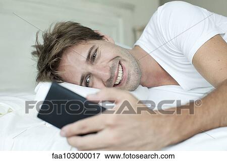 Stock Photo - Man in bed using smartphone. Fotosearch
