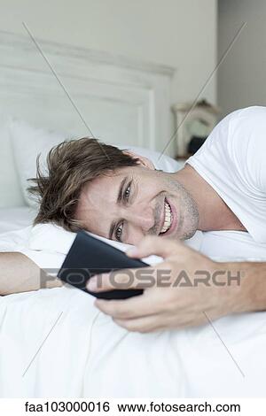 Man in bed using smartphone View Large Photo Image Stock Photograph - Man in bed using smartphone. Fotosearch