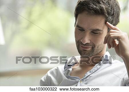 Man looking down attentively with finger pressed against temple View Large Photo Image Stock Image - Man looking down attentively with finger pressed against temple. Fotosearch