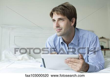 "Man lying in bed using digital tablet, looking away with contemplative look" View Large Photo Image Stock Image - "Man lying in bed using digital tablet, looking away with contemplative look". Fotosearch