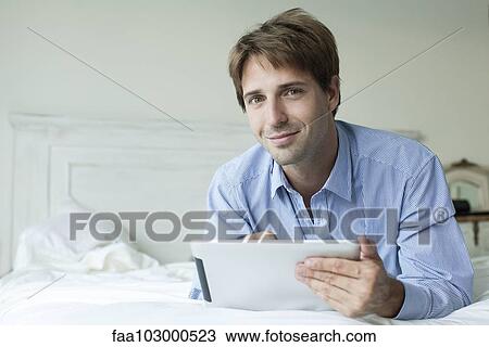 Man lying in bed using digital tablet View Large Photo Image Stock Image - Man lying in bed using digital tablet. Fotosearch