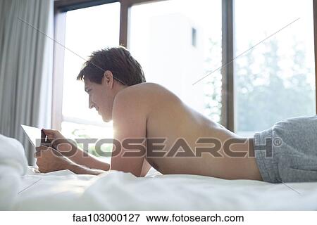 Man lying in bed using digital tablet View Large Photo Image Stock Photo - Man lying in bed using digital tablet. Fotosearch