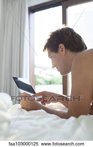Man lying in bed using digital tablet View Large Photo Image Stock Photography - Man lying in bed using digital tablet. Fotosearch