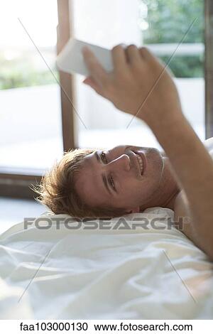Man lying in bed using multimedia smartphone to video conference View Large Photo Image Stock Image - Man lying in bed using multimedia smartphone to video conference. Fotosearch