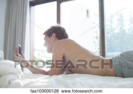 Man lying in bed using multimedia smartphone View Large Photo Image Stock Photo - Man lying in bed using multimedia smartphone. Fotosearch