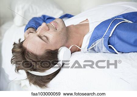 Man lying on bed listening to music with headphones View Large Photo Image Stock Photo - Man lying on bed listening to music with headphones. Fotosearch