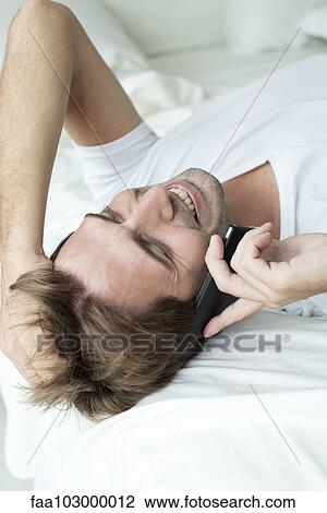 "Man lying on bed, talking on cell phone" View Large Photo Image Stock Image - "Man lying on bed, talking on cell phone". Fotosearch