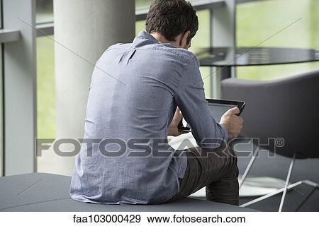 "Man sitting alone, looking at digital tablet, rear view" View Large Photo Image Stock Photo - "Man sitting alone, looking at digital tablet, rear view". Fotosearch