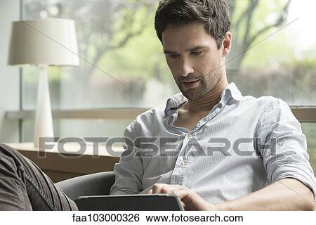 Stock Photograph - Man using digital tablet at home. Fotosearch