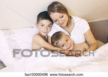 Stock Photo - "Mother and young sons together on bed, portrait". Fotosearch
