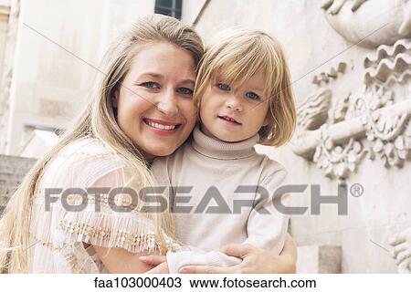 Stock Image - "Mother embracing young daughter outdoors, portrait". Fotosearch