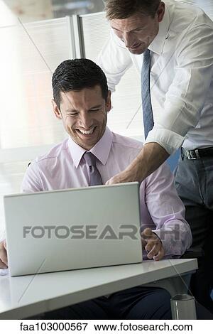 Stock Photo - Office workers looking at computer together laughing. Fotosearch