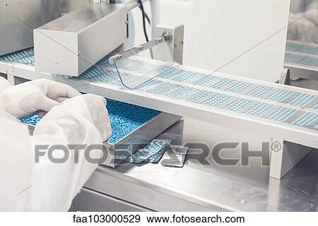 Stock Photo - Technician monitoring pills on conveyor belt entering blisterpack sealing machine. Fotosearch