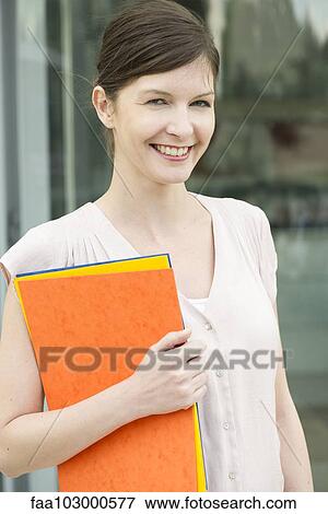 "Woman carrying folders, smiling cheerfully, portrait" View Large Photo Image Stock Photo - "Woman carrying folders, smiling cheerfully, portrait". Fotosearch