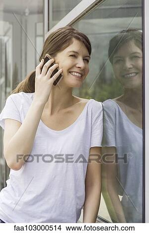 Woman leaning against window talking on cell phone View Large Photo Image Picture - Woman leaning against window talking on cell phone. Fotosearch