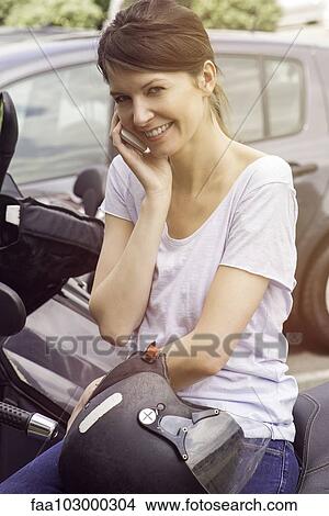 "Woman sitting on parked motorcycle, talking on cell phone" View Large Photo Image Picture - "Woman sitting on parked motorcycle, talking on cell phone". Fotosearch