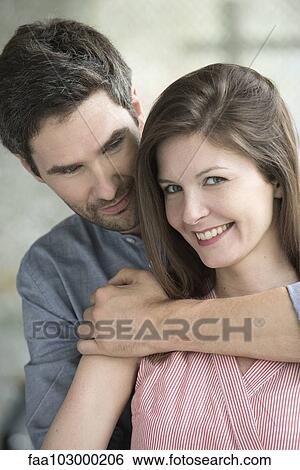 "Woman smiling as husband embraces her, portrait" View Large Photo Image Stock Photograph - "Woman smiling as husband embraces her, portrait". Fotosearch