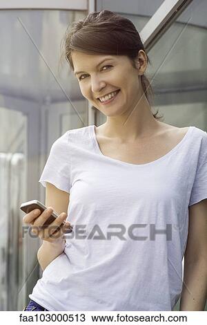 Stock Image - "Woman using smartphone outdoors, smiling cheerfully". Fotosearch