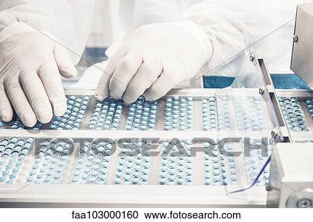 Stock Image - Worker inspecting pills on blisterpack conveyer belt. Fotosearch