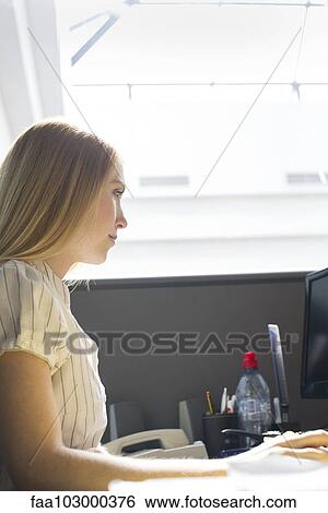 Stock Photograph - Young woman working intently in office cubicle. Fotosearch