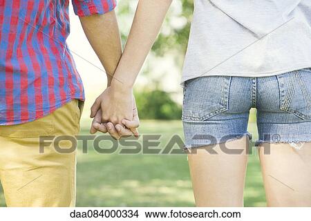 Couple holding hands outdoors, cropped rear view View Large Photo Image Picture - Couple holding hands outdoors, cropped rear view. Fotosearch