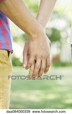 Stock Photo - Couple holding hands outdoors, cropped rear view. Fotosearch