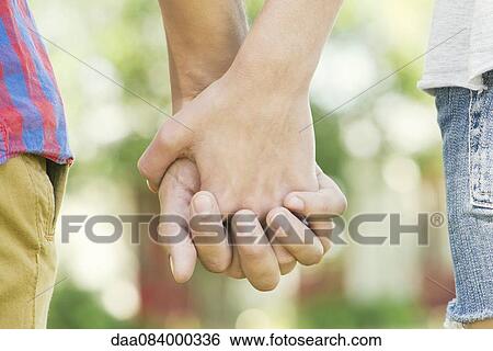 Couple holding hands outdoors, cropped rear view View Large Photo Image Stock Photograph - Couple holding hands outdoors, cropped rear view. Fotosearch