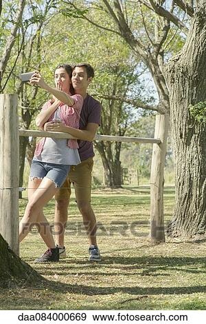 Couple posing for a selfie in park View Large Photo Image Stock Photo - Couple posing for a selfie in park. Fotosearch