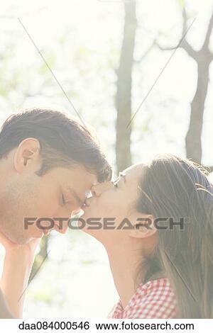 Stock Photograph - Couple together outdoors, woman kissing man's forehead. Fotosearch