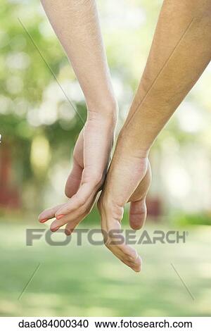 Stock Image - Couple touching hands outdoors, cropped rear view. Fotosearch