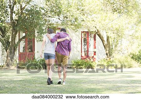 Couple walking outdoors with arms around each other's shoulders, rear view View Large Photo Image Stock Image - Couple walking outdoors with arms around each other's shoulders, rear view. Fotosearch