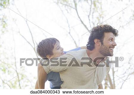Stock Image - Father carrying young son piggyback. Fotosearch
