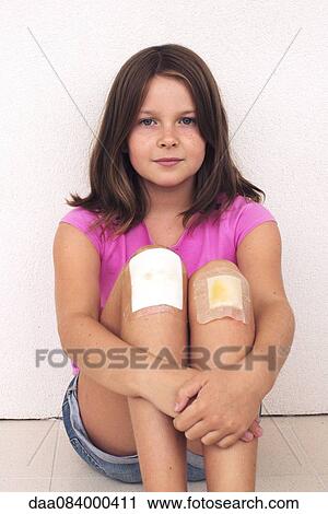 Stock Image - Girl hugging bandaged knees, portrait. Fotosearch