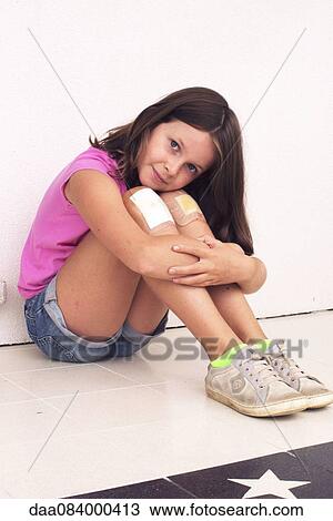 Stock Image - Girl hugging bandaged knees, portrait. Fotosearch