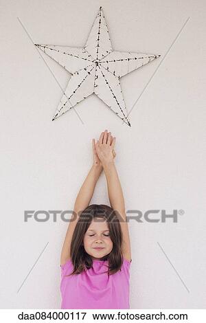 Girl reaching toward star shape hanging above her head, eyes closed View Large Photo Image Stock Photo - Girl reaching toward star shape hanging above her head, eyes closed. Fotosearch