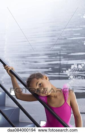 Picture - Little girl in ballerina costume leaning against staircase railing. Fotosearch