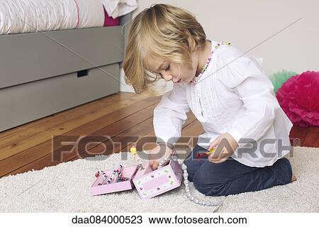 Stock Image - Little girl removing necklace from jewellery box. Fotosearch