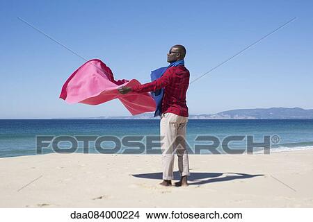 Man at the beach, holding blanket in the breeze View Large Photo Image Picture - Man at the beach, holding blanket in the breeze. Fotosearch