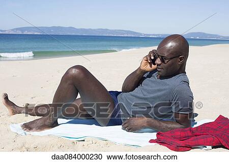 Man lying on beach, talking on cell phone View Large Photo Image Stock Image - Man lying on beach, talking on cell phone. Fotosearch