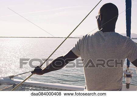 Stock Photo - Man on sail boat, looking at view. Fotosearch