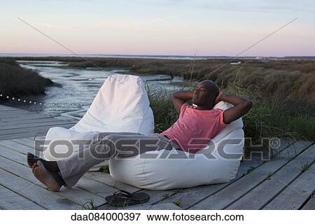 Stock Photo - Man relaxing on dock at water's edge. Fotosearch