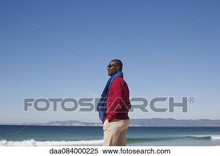 Stock Photography - Man standing alone on beach, looking at view. Fotosearch