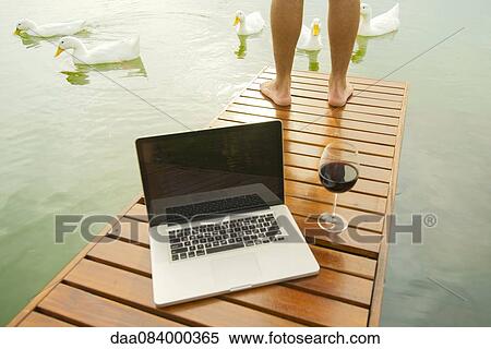 Man standing on lake dock, laptop computer and wine glass in foreground View Large Photo Image Stock Photography - Man standing on lake dock, laptop computer and wine glass in foreground. Fotosearch