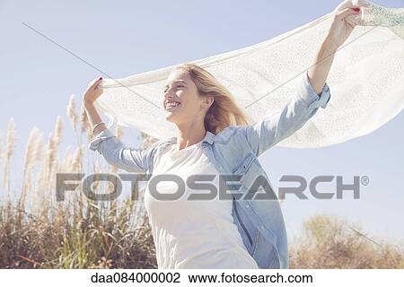 Stock Image - Woman holding up scarf fluttering in wind. Fotosearch