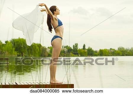 Woman in bikini standing at end of lake pier, holding scarf in the breeze View Large Photo Image Stock Photography - Woman in bikini standing at end of lake pier, holding scarf in the breeze. Fotosearch