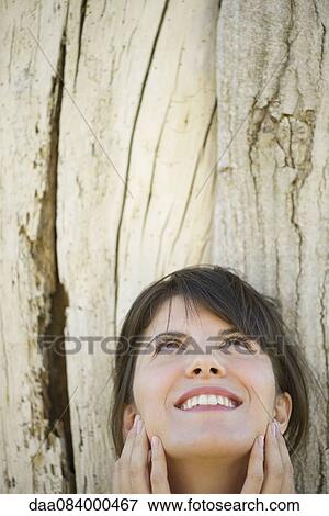 Woman leaning against tree trunk, looking up and smiling View Large Photo Image Stock Photo - Woman leaning against tree trunk, looking up and smiling. Fotosearch
