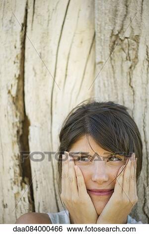 Woman leaning against tree trunk, smiling and holding face in hands, portrait View Large Photo Image Stock Photograph - Woman leaning against tree trunk, smiling and holding face in hands, portrait. Fotosearch