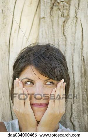 Woman leaning against tree trunk, smiling and holding face in hands, portrait View Large Photo Image Stock Photography - Woman leaning against tree trunk, smiling and holding face in hands, portrait. Fotosearch
